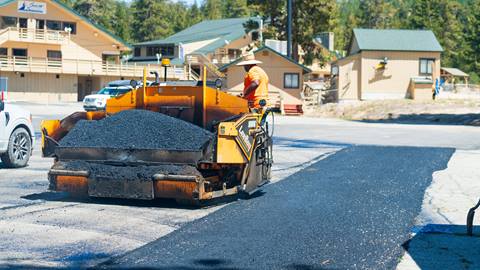 Construction worker in Snow Valley parking lot on asphalt paver next to new asphalt.