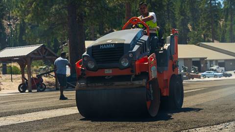 Adult driving asphalt roller at Snow Valley rolling and smoothening new parking lot.