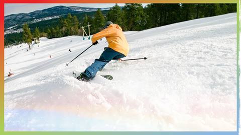 Skier in a yellow jacket and blue pants carving down the slopes
