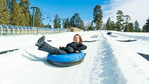 An adult in a snow tube at Snow Valley's Coyote Creek Tube Park riding down a tubing lane