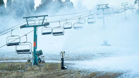 A shot of the chairlift and run while snow guns cover the ski hill.