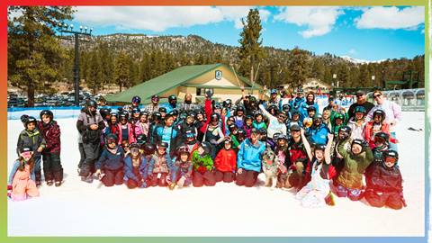 A group of 20+ kiddos plus adults smiling at the camera while in ski clothes during a sunny day at Snow Valley