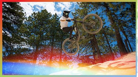 A mountain biker in black pants, a white jersey, black bike and full face helmet catching air off a dirt jump at Snow Valley.