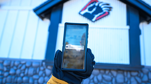 Mobile App on a phone in front of Bear Mountain's bear claw logo