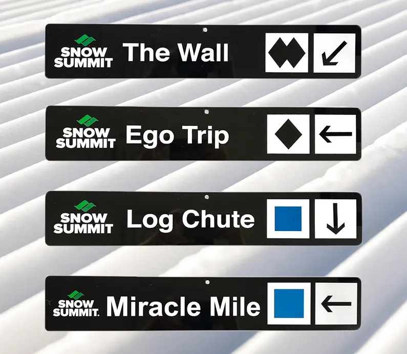 Black trail signs with Snow Summit winter runs: The Wall, Ego Trip, Log Chute, Miracle Mile.