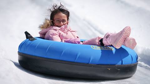 Adult in pink jacket and pink boots in a snow tube at Snow Valley's Coyote Creek Tube Park