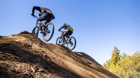 Two cyclists mid-air riding over dirt jump
