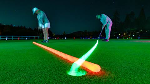 Two adult golfers at night putting glow in the dark colorful balls into the hole at Bear Mountain Golf Course