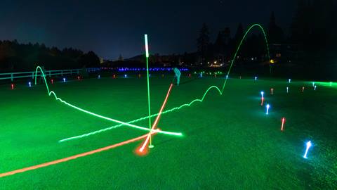 A golfer on the putting green at night during a Glow Golf evening at Bear Mountain Golf Course hitting a red glow ball into the hole