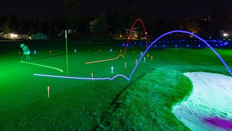 A Glow Golf night at Bear Mountain Golf Course with an adult on a lit up putting green putting a green ball into the hole.