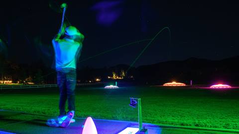 A golfer at the glow in the dark driving range practicing target practice and hitting to the glow holes