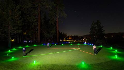 An evening under the stars at Bear Mountain Golf Course while three golfers put glowing golf balls to a hole while green glow lights illuminate the green.