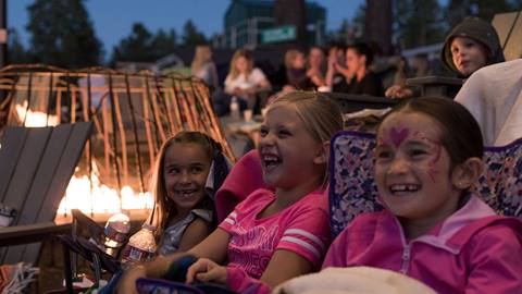 Three kiddos with big smiles on their faces watching a movie at a Movies in the Meadow event at Snow Summit