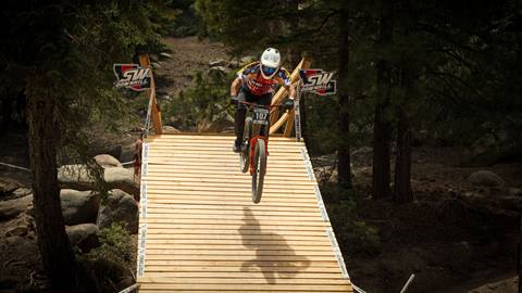 A mountain bike rider jumping down a wooden bridge terrain feature during the Southwest Downhill race at Snow Valley.