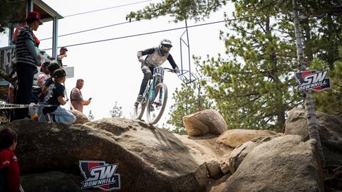 Spectators at Snow Valley's Southwest Downhill bike race watching a mountain bike rider in a full face white helmet and white jersey ride through a rock garden.