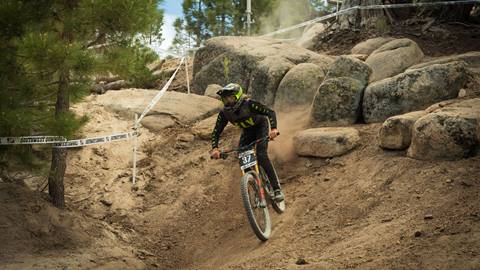 A mountain bike rider in all black with a full face helmet finishing a rock section on a dirt trail during the Southwest Downhill event at Snow Valley.