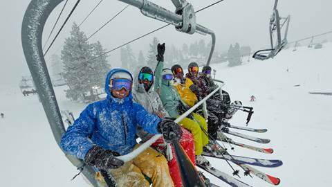 A group of six skiers on a stormy snow day at Snow Valley riding up the high speed Snow Valley Express chairlift.