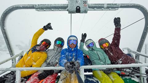 A group of five skiers on a stormy snow day at Snow Valley riding up the high speed Snow Valley Express chairlift.