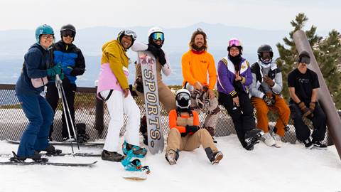 A group of nine skiers and snowboarders posing for the camera in full winter attire during a sunny yet hazy day at Snow Valley.