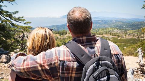 Two adult hikers, one with a long sleeve flannel and black backpack, looking into the distance and appreciating the Snow Valley views on a sunny blue day.