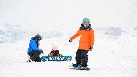 Two kiddos on snowboards with a Big Bear Mountain Resort snowboard instructor strapping in to shred