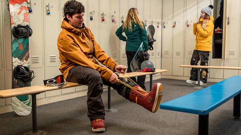 Group of people in a locker room, guy putting on boots