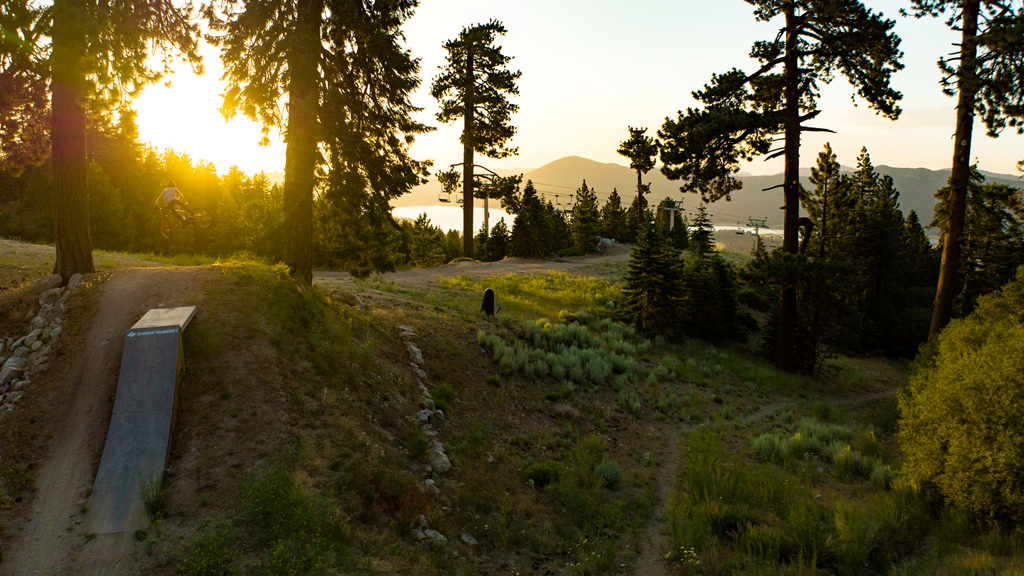 Mountain biker going off a ramp with a green scenery and sunset in the background