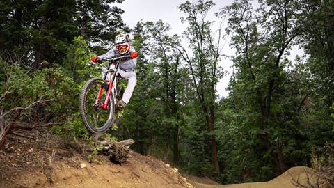 A mountain biker catching air off a dirt jump at Snow Summit wearing red gloves and top to bottom white apparel on a red and white bike.
