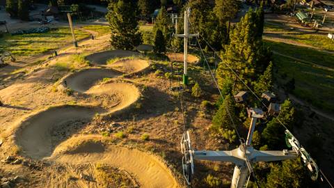 A drone image hovering over a chairlift at Snow Summit with a dirt snake run trail to the left.