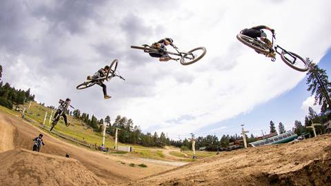 A sequence image of a mountain biker going off a large dirt jump at the base area of Summit Bike Park with one foot off their pedal.