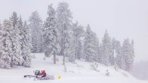 Snow day on the slopes with a snow cat grooming a trail