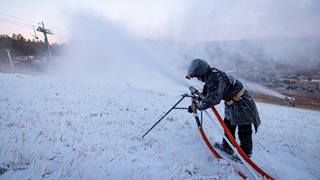 Snowmaking team member checking snowgun that's blowing snow onto hill.